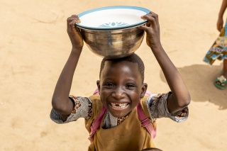 Young boy balancing silver bowl on his head smiling at camera